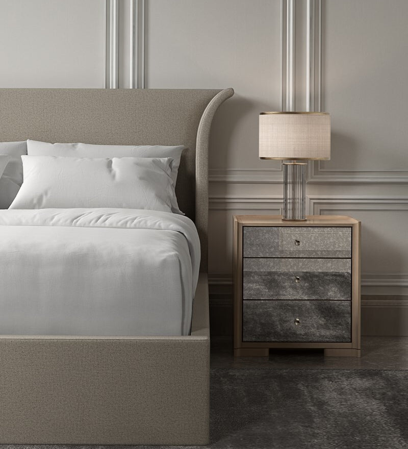 Neatly made bed with a nightstand featuring a lamp in a bedroom setting.